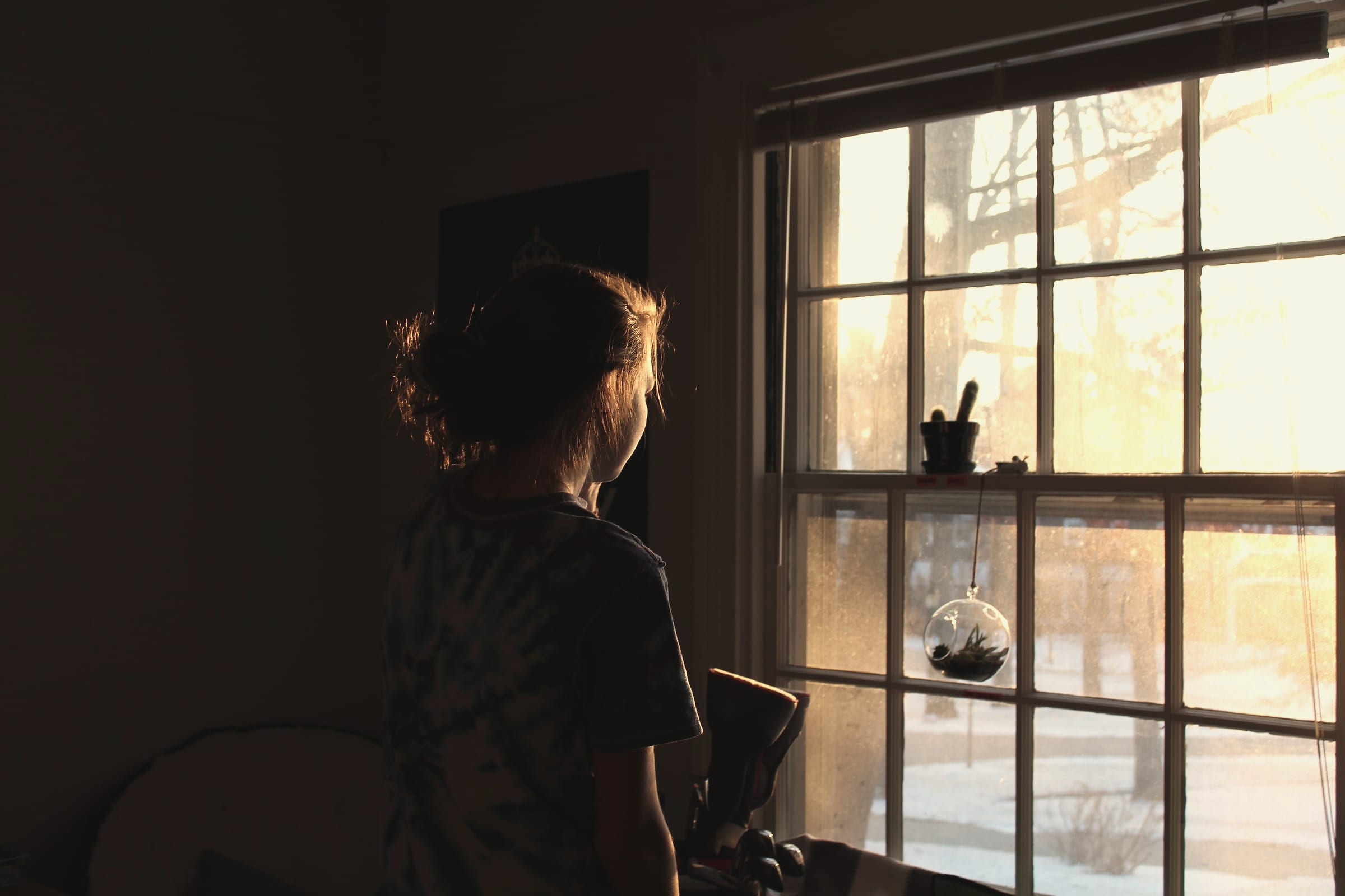 A person seen from behind sits beside a sunlit window in a quiet room.